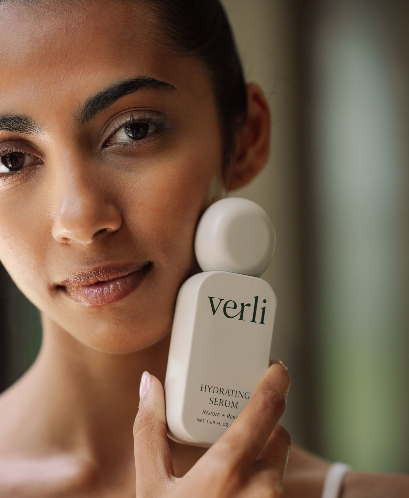 Woman holding a Verli hydrating serum bottle close to her face