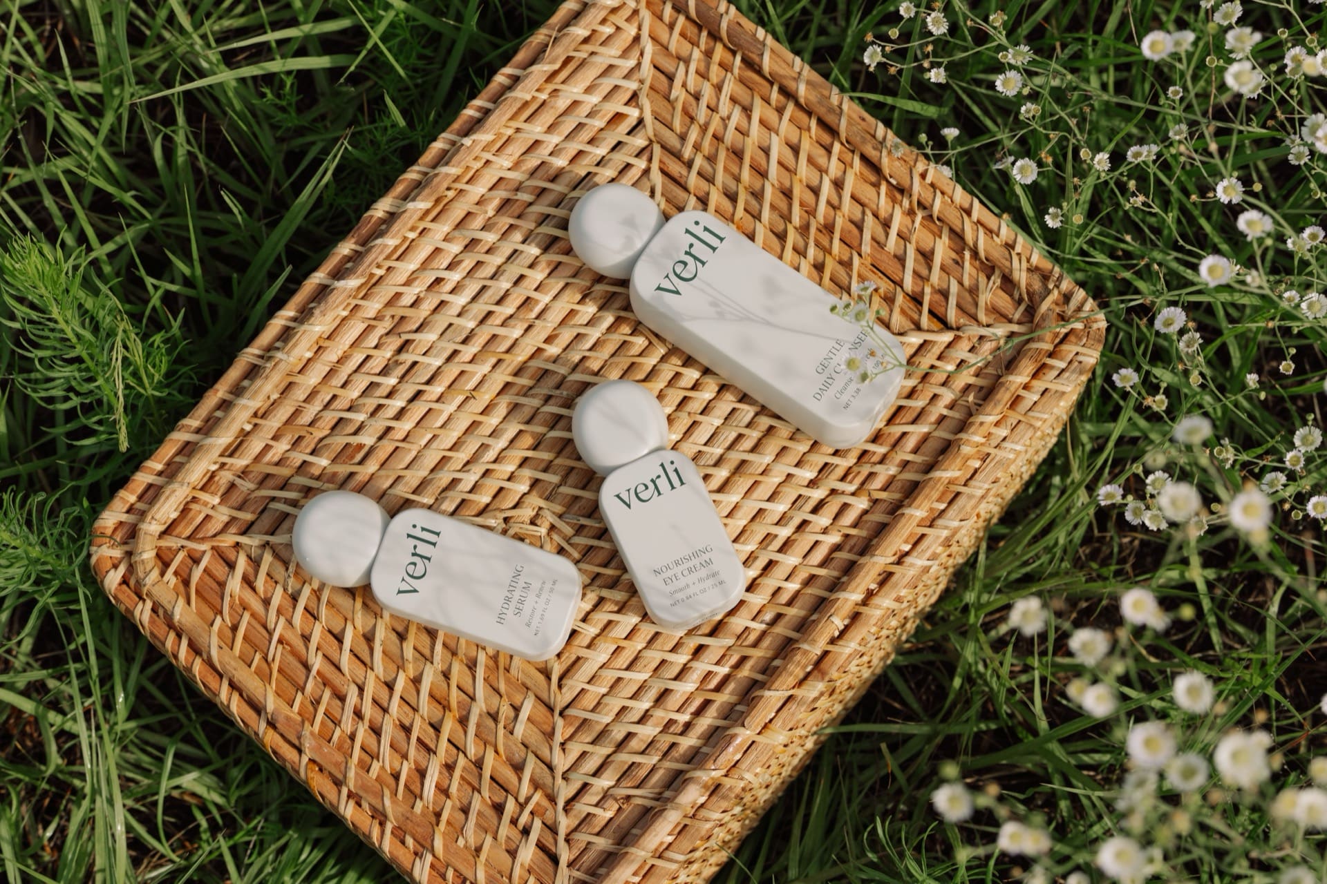 Verli skincare products on a woven tray with grass and flowers in the background